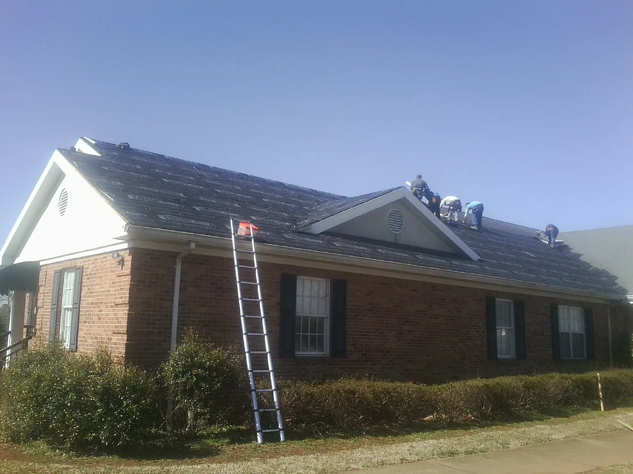 Crew tearing shingles off a brick ranch roof with a ladder set — Emergency Roof Repair work by our crew in Normandy