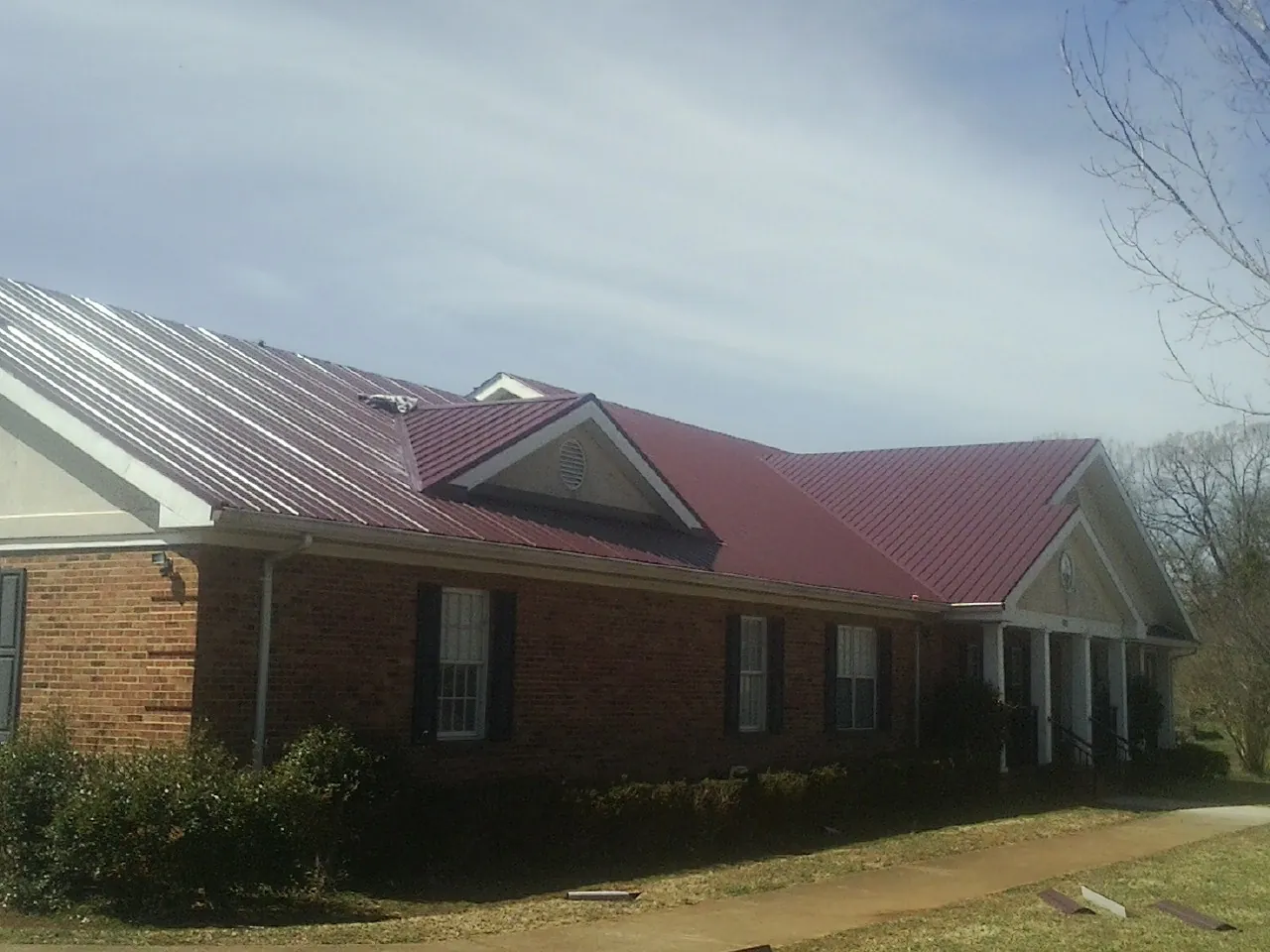 Red metal roof with gabled entries on a long brick building, from a Hail Damage Roof Repair job in Normandy