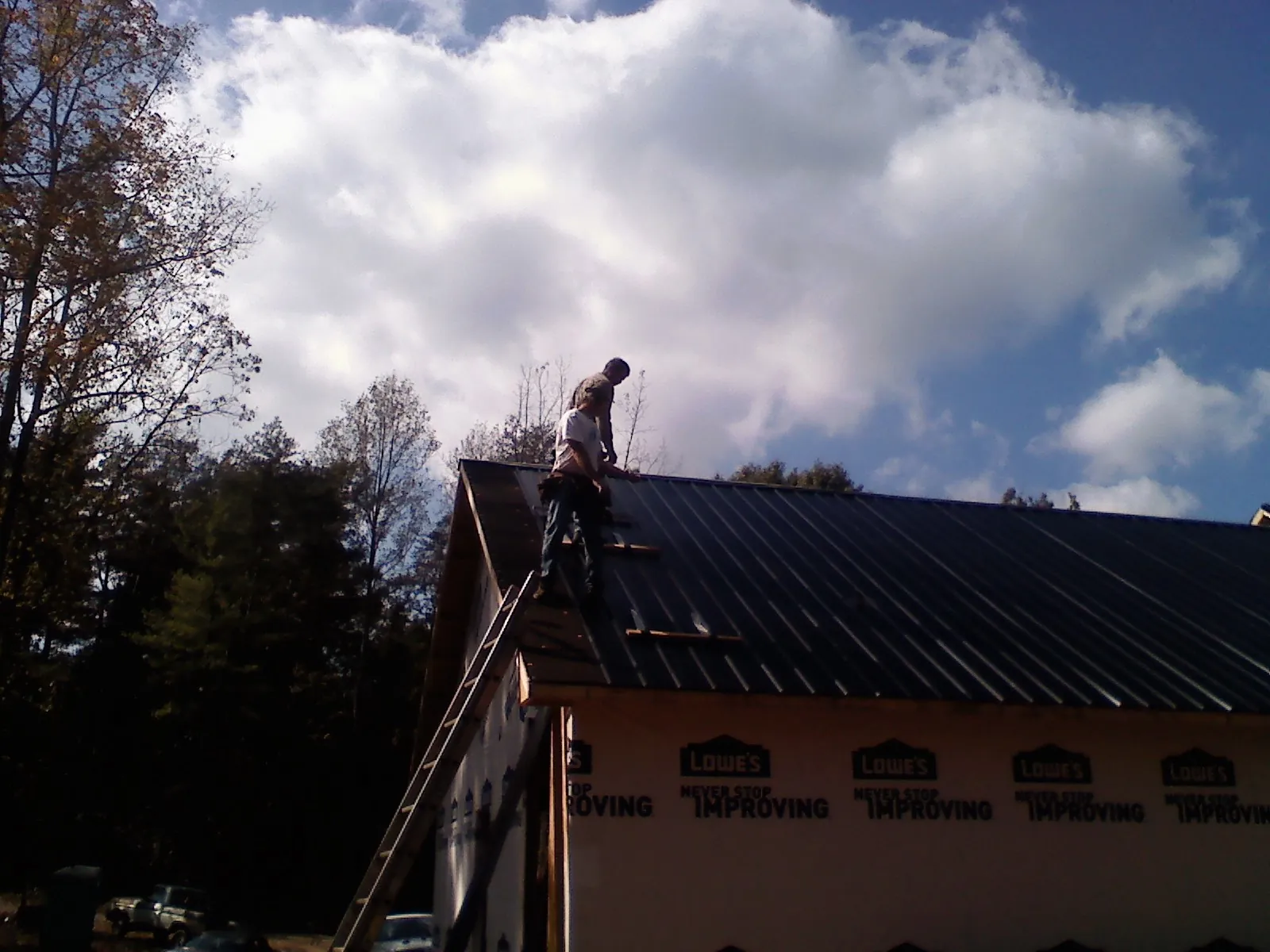 Roofer fastening dark metal panels high against a cloudy sky, from a Roof Inspection job in Normandy
